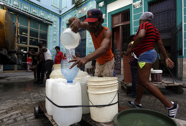 A man fills containers with water from a tanker truck on a street in Old Havana, in the Cuban capital. Water supply problems in households caused by structural problems in the water grid and severe drought have complicated the lives of people in Havana, and especially those of women. Credit: Jorge Luis Baños/IPS