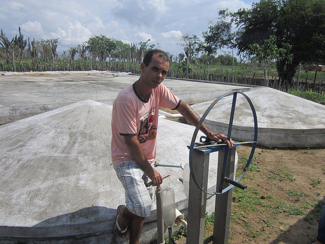 Abel Manto stands next to the closed water tanks built to collect rainwater and irrigate his vegetable gardens in the Northeastern Brazilian state of Bahia. The green on this farmer and inventor’s land stands in sharp contrast with the aridity of the region, while the lids on his tanks keep mosquitoes from breeding in the water. Credit: Mario Osava/IPS