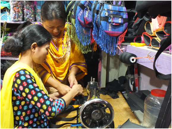 Cheya  Chakma (in yellow dress) showing an employee how to fine tune some stitching. Credit: Naimul Haq /IPS