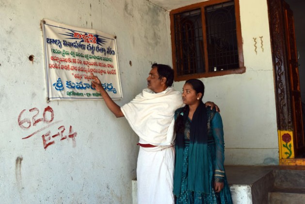 Indian Hindu priest Shri Kumar Sharma and his daughter Bhargavi read an anti-child marriage poster that says anyone found guilty of a child marriage can get 2 years of jail and fined Rs 100,000 ( US$1,470). Credit: Stella Paul/IPS