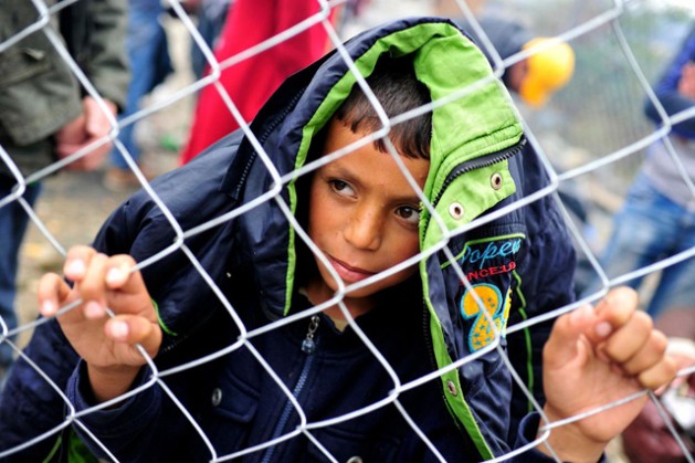 A boy clutches and looks through a chain-link fence, on a rainy day near the Former Yugoslav Republic of Macedonia town of Gevgelija, on the border with Greece. September 2015 . Credit: UNICEF/UNI196199/Georgiev