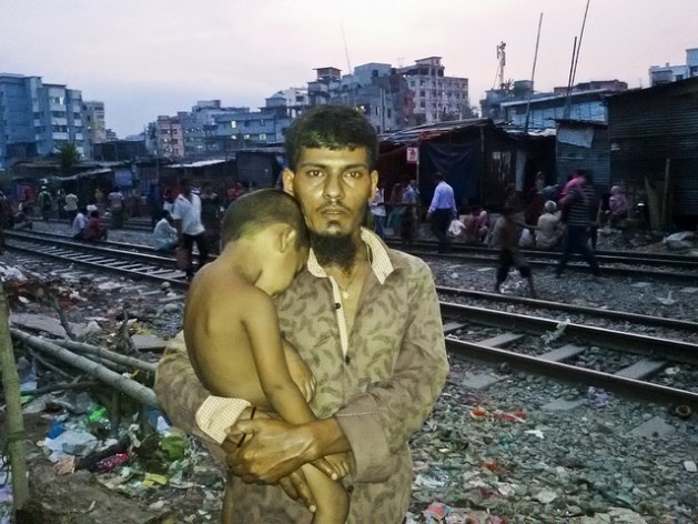 Abdul Aziz stands with one of his children in Dhaka's Malibagh slum. He came here a decade ago after losing everything to river erosion, hoping to rebuild his life, but has found only grinding poverty. Credit: Rafiqul Islam/IPS