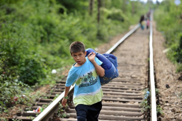 A boy carrying his belongings in a large cloth bag over his shoulder is among people walking on railway tracks to cross from the Former Yugoslav Republic of Macedonia into Serbia. Photo: UNICEF/NYHQ2015-2203/Georgiev