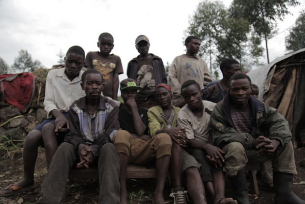 A group of young Mbuti men from Biganiro, DRC, sit in front of their houses, which consist of makeshift structures made of wood and plastic sheeting. Credit: Zahra Moloo/IPS