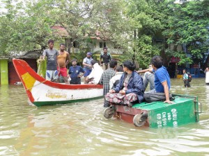 A couple wait on an overturned garbage bin to be rescued by boat during the Chennai flooding of December 2015. Credit: R. Samuel/IPS