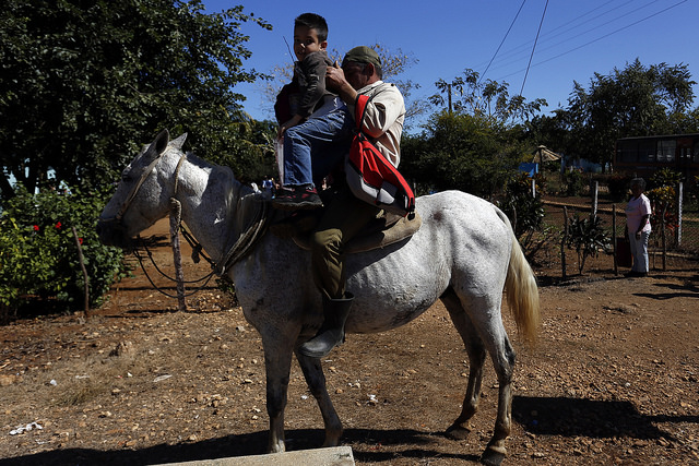 A father settles his son on his horse, as he picks him up from school in a rural community in the central province of Villa Clara, Cuba. The new legislation to stimulate maternity in the country doesn’t pay any attention to fathers, according to experts. Credit: Jorge Luis Baños/IPS