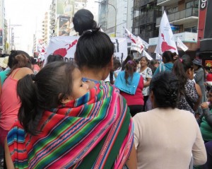 A migrant from an Andean country, carrying her daughter on her back, demonstrates for her rights along with other migrant women, in Buenos Aires, during a Mar. 24 march marking the anniversary of the 1976 military coup that ushered in seven years of dictatorship. Credit: Fabiana Frayssinet/IPS